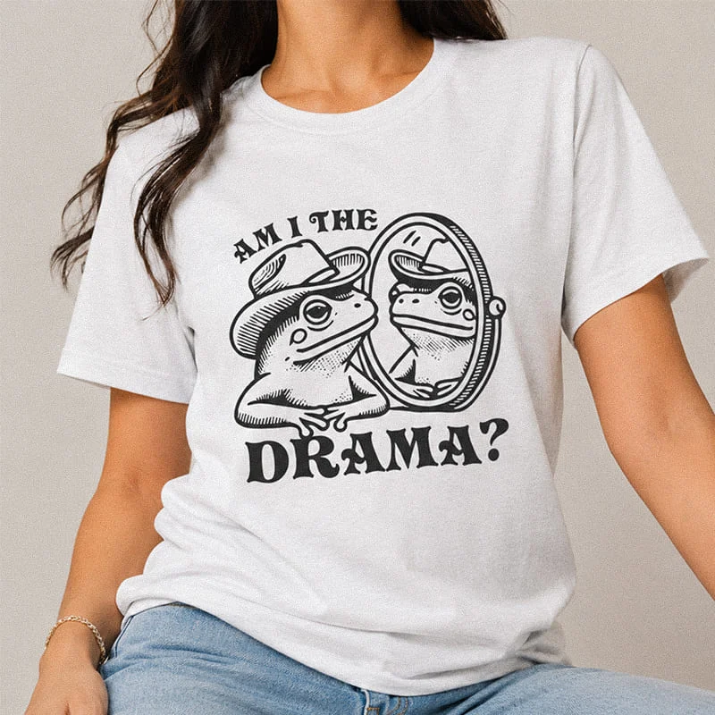 Woman wearing a white t-shirt featuring a cartoon toad in a cowboy hat looking into a mirror with the text "Am I The Drama?"
