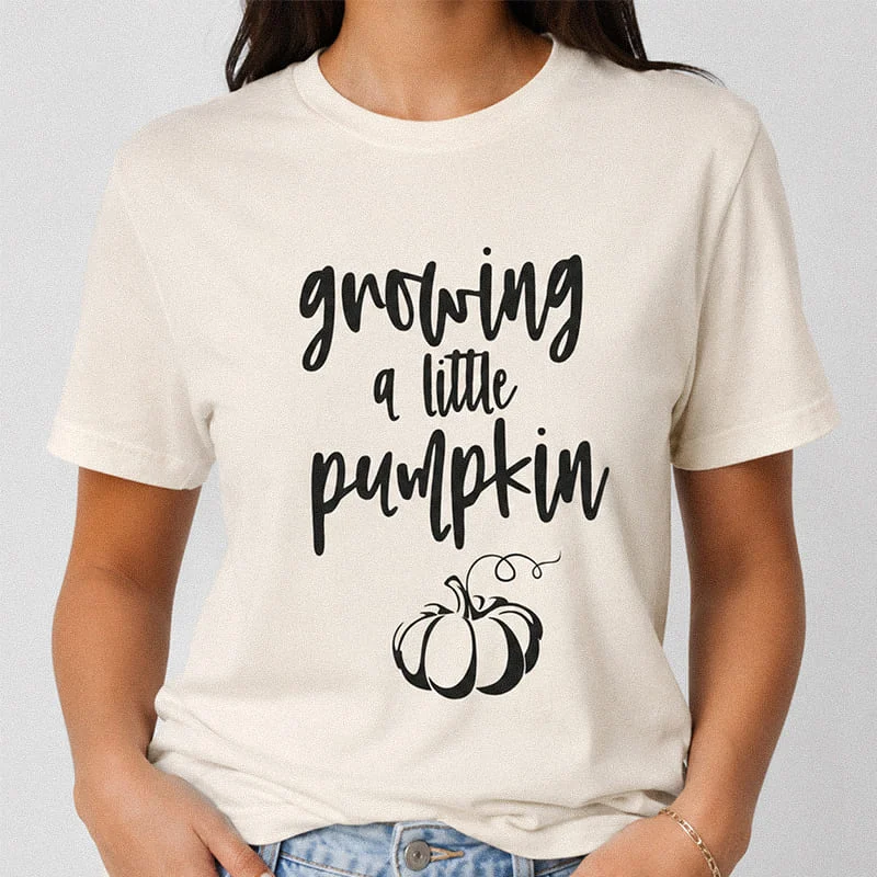 Woman wearing a natural Growing a Little Pumpkin Shirt - Pregnancy Halloween Shirt with cursive typography and a cute pumpkin illustration