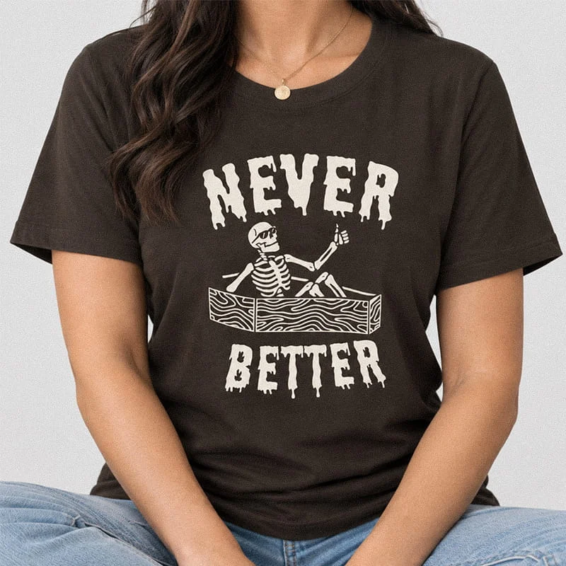 Person wearing a dark brown Never Better Skeleton T-Shirt - Funny Skull Graphic Tee featuring a skeleton wearing sunglasses giving a thumbs up from inside a coffin