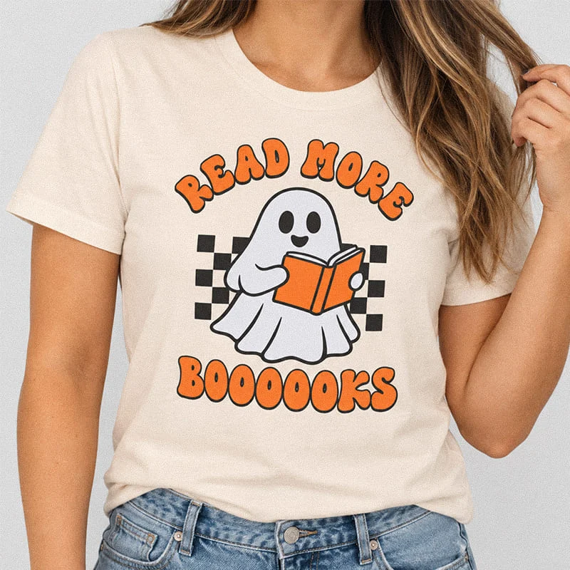 Woman wearing a soft cream Read More Booooks Shirt - Halloween Reading Ghost Tee with a cute ghost reading a book over a checkered graphic reading Read More Boooooks