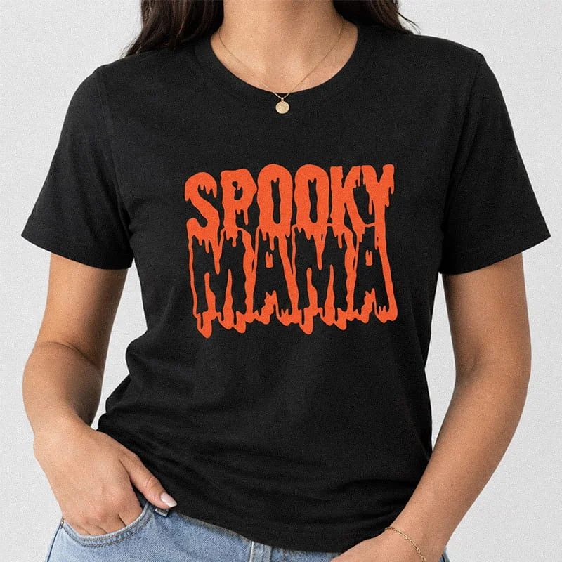 Woman wearing a black Spooky Mama T-Shirt - Retro Halloween Graphic Tee for Moms featuring the phrase Spooky Mama rendered in a bold orange dripping font