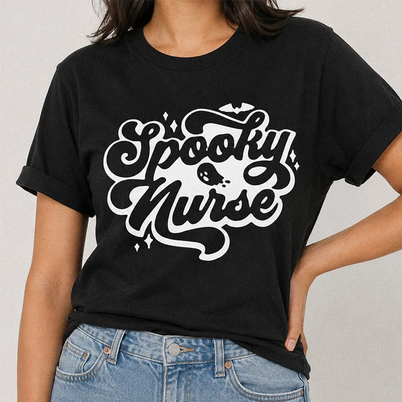 Woman wearing a black Spooky Nurse Shirt – Funny Halloween Nurse Tee featuring retro cursive typography reading Spooky Nurse with a cute ghost illustration