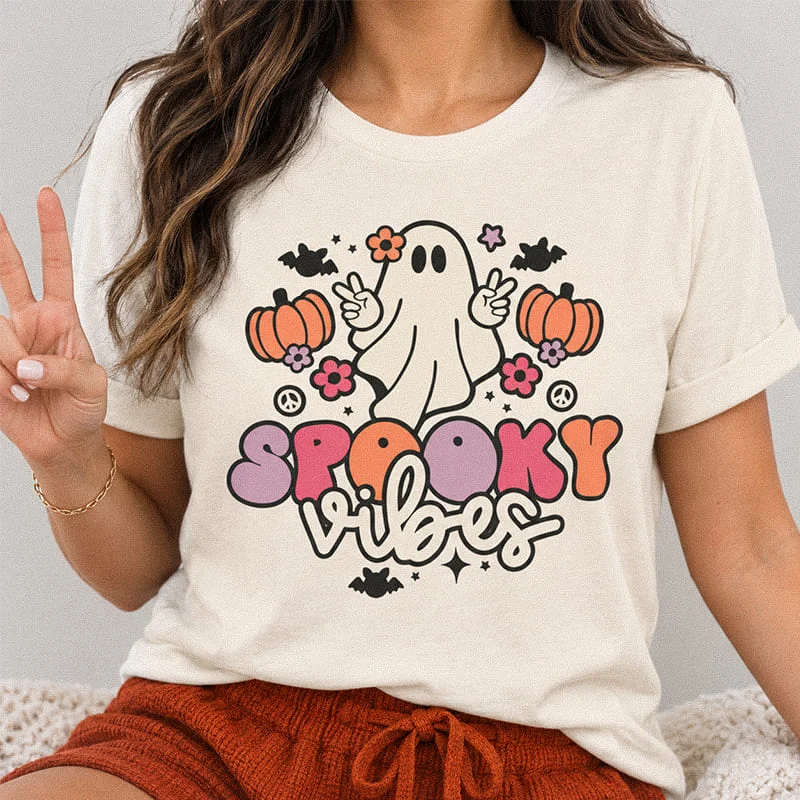 Woman wearing a natural color Spooky Vibes Halloween Ghost Shirt – Cute Spooky Season Tee featuring a peace-sign ghost, pumpkins, flowers, and typography reading Spooky Vibes