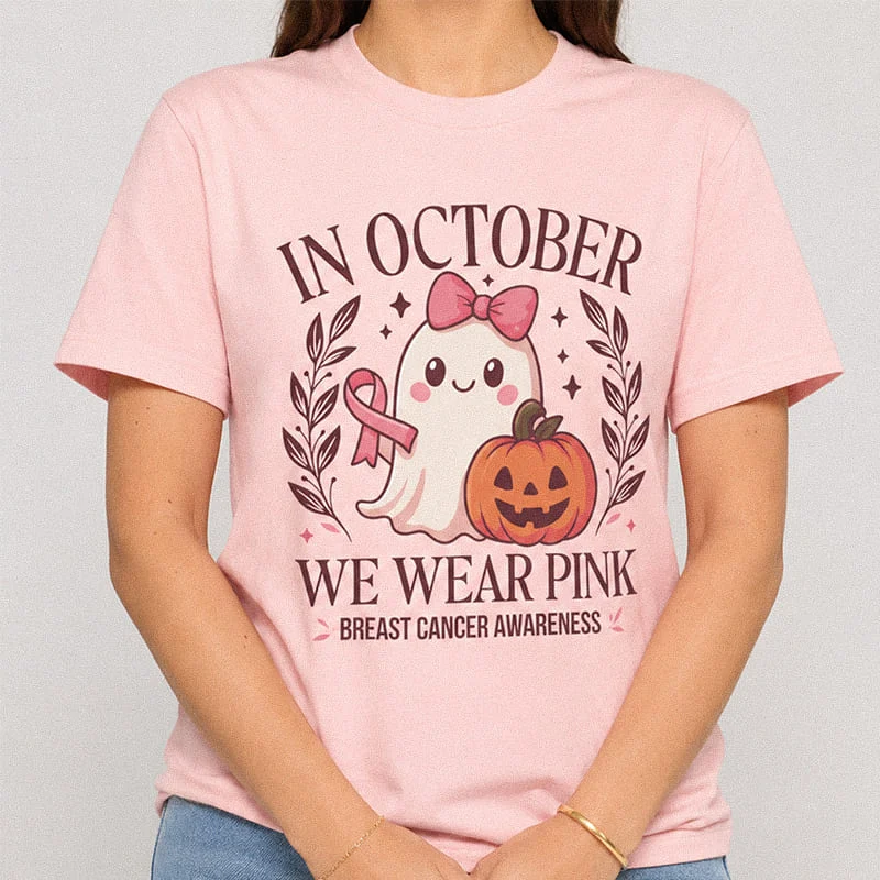 Woman wearing a light pink In October We Wear Pink Shirt - Breast Cancer Awareness Halloween Tee featuring a cute ghost with a pink bow ribbon and a jack-o'-lantern pumpkin