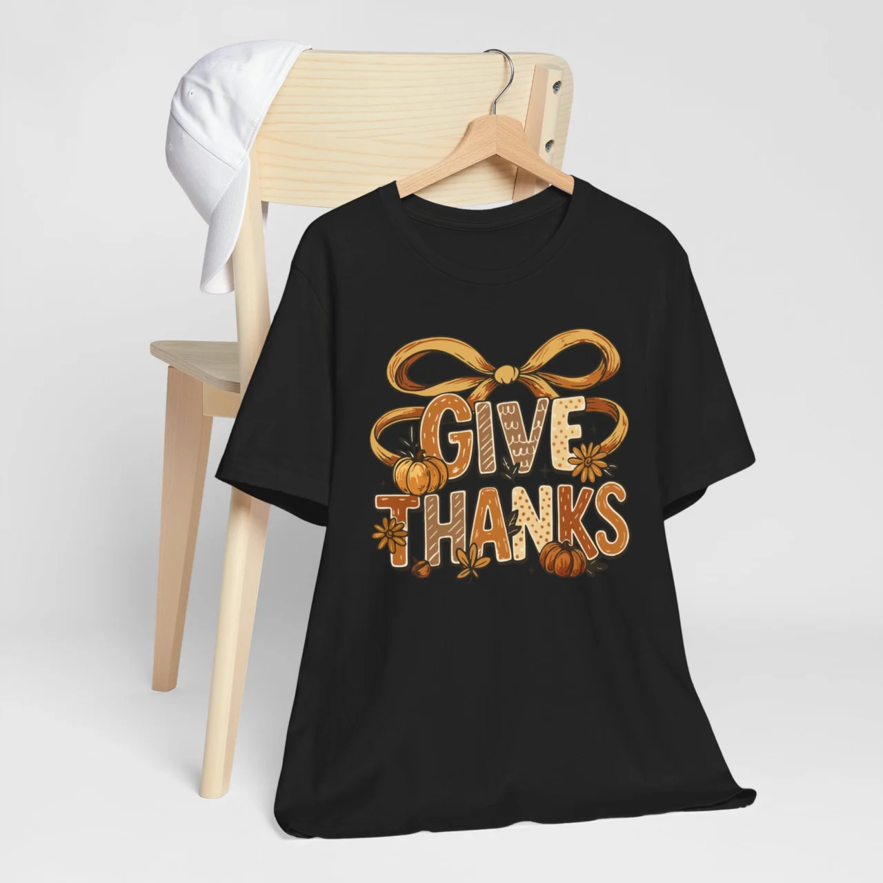 Give Thanks Shirt with a rustic gold ribbon and fall-themed lettering, featuring pumpkins and flowers, on a black t-shirt, a cozy Thanksgiving design.