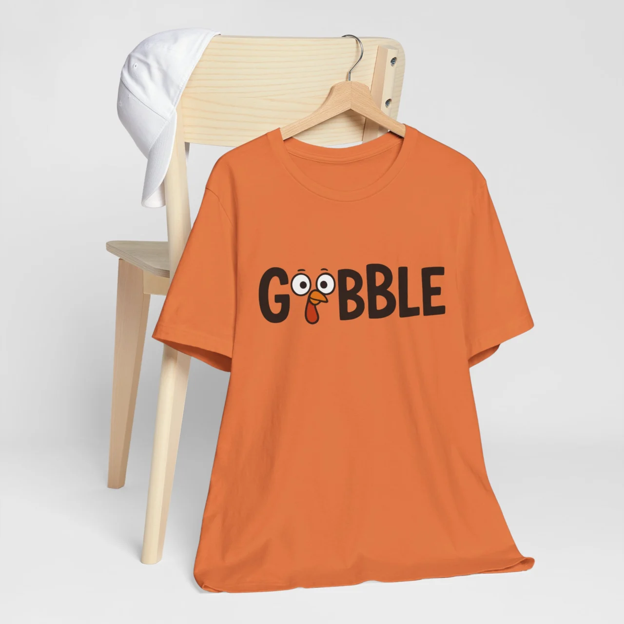 GOBBLE Shirt with a cartoon turkey face integrated into the lettering, on a vibrant orange t-shirt, a simple and funny Thanksgiving t-shirt
