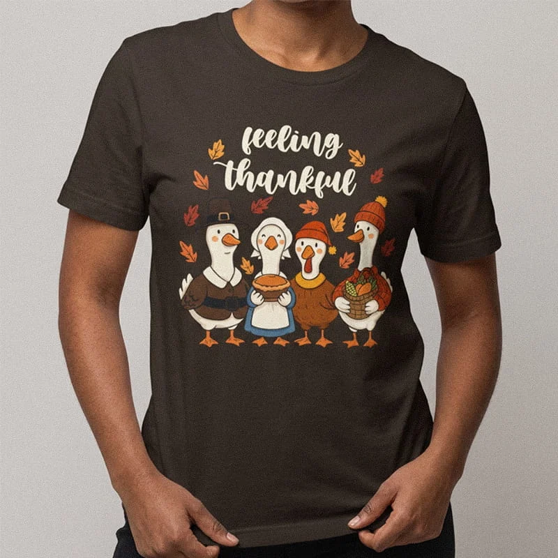 Person wearing a dark brown Feeling Thankful Geese Shirt - Cute Thanksgiving Pilgrim T-Shirt featuring four dressed-up geese carrying autumn food with text reading Feeling Thankful