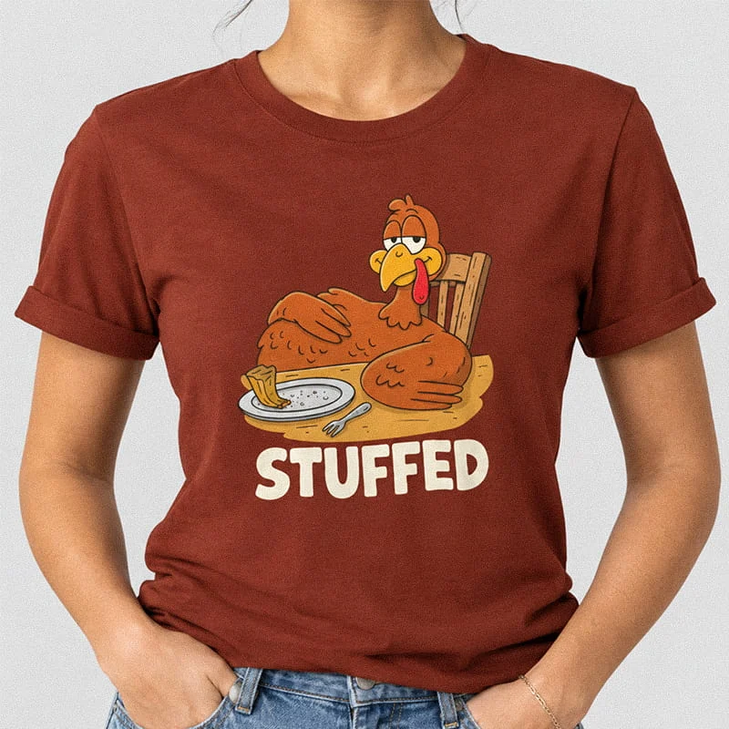 Woman wearing a rust STUFFED Turkey Shirt - Funny Thanksgiving Food Coma T-Shirt featuring a full cartoon turkey sitting back at a dinner table next to an empty plate above text reading Stuffed