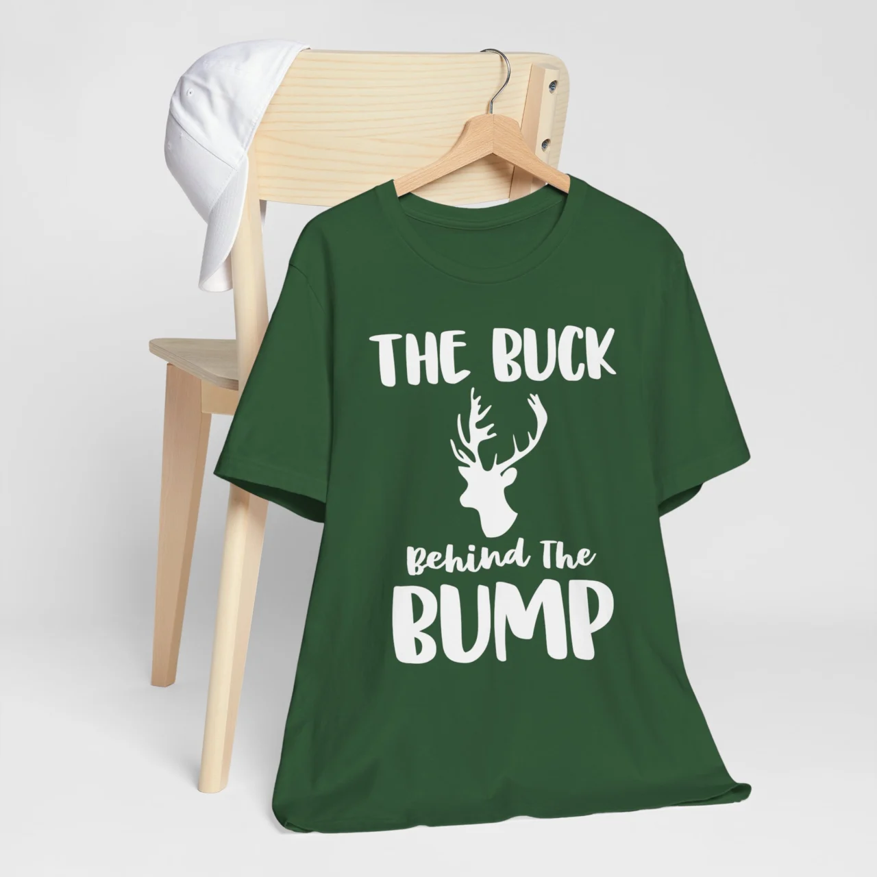 The Buck Behind the Bump Shirt in dark green with a white deer silhouette and text, a Dad Matching Christmas Announcement Tee design.