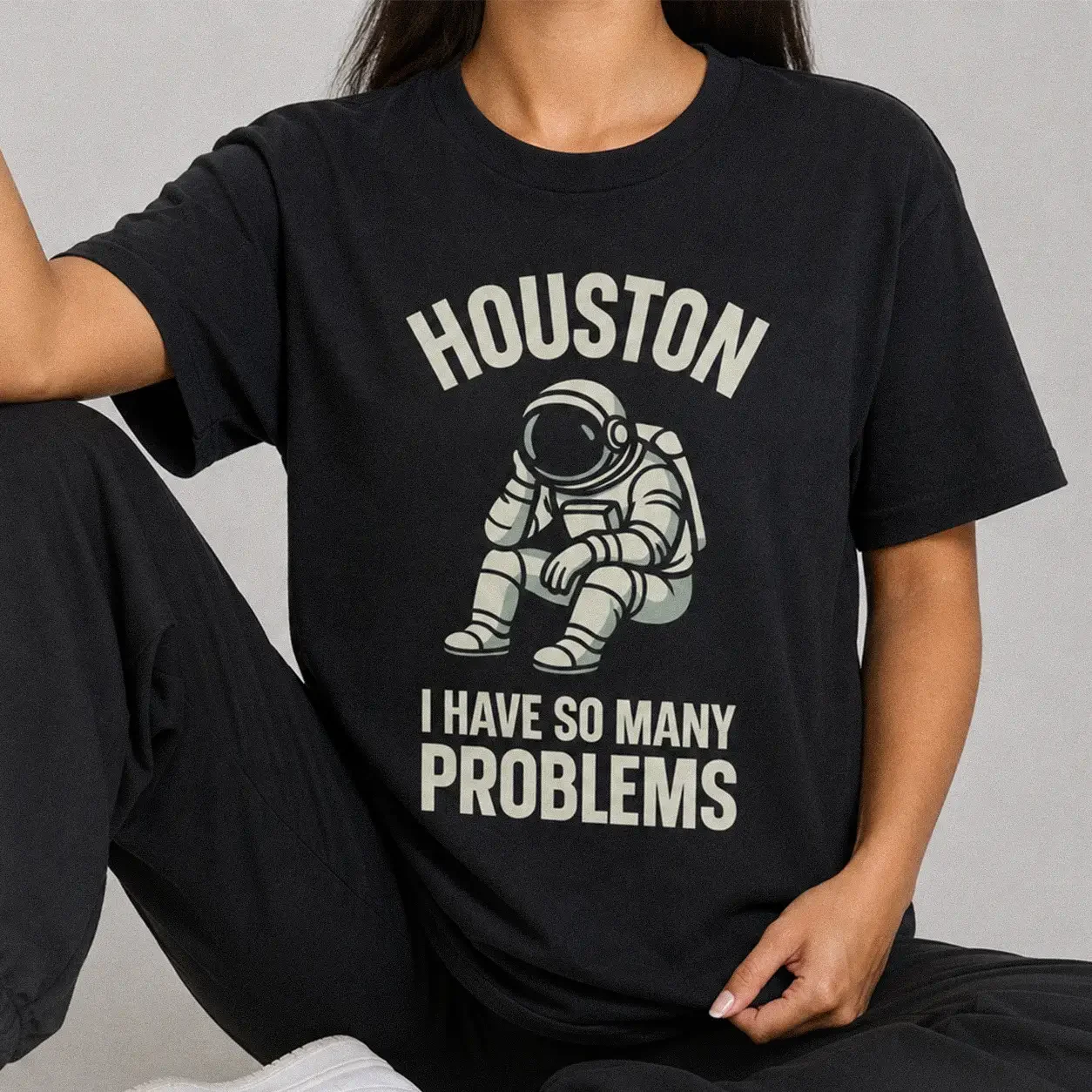 Woman wearing a black Houston I Have So Many Problems Astronaut Tee featuring a funny illustration of a sitting astronaut resting their head and the text "Houston I Have So Many Problems"