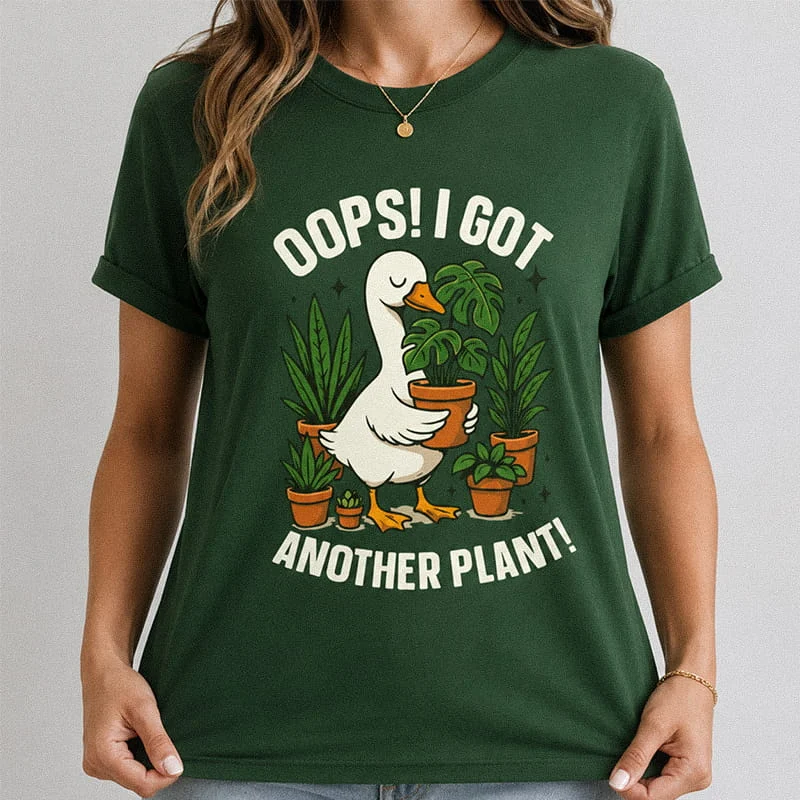 Woman wearing a dark green Oops I Got Another Plant Funny Plant Mom Tee featuring a cartoon duck holding a potted plant surrounded by houseplant pots with the text "Oops! I Got Another Plant!"